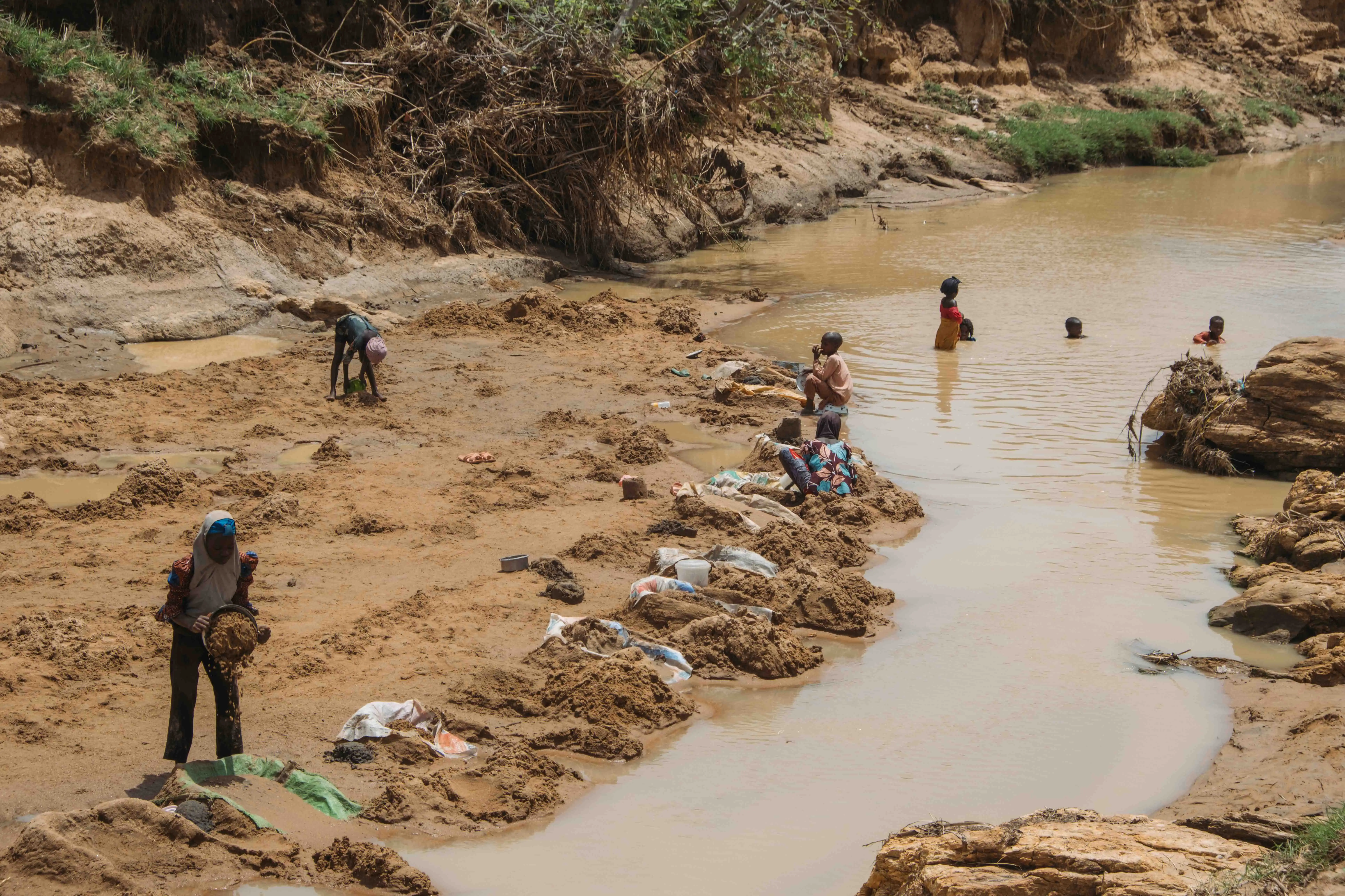 Young miners panning for teli along a muddy riverbed
