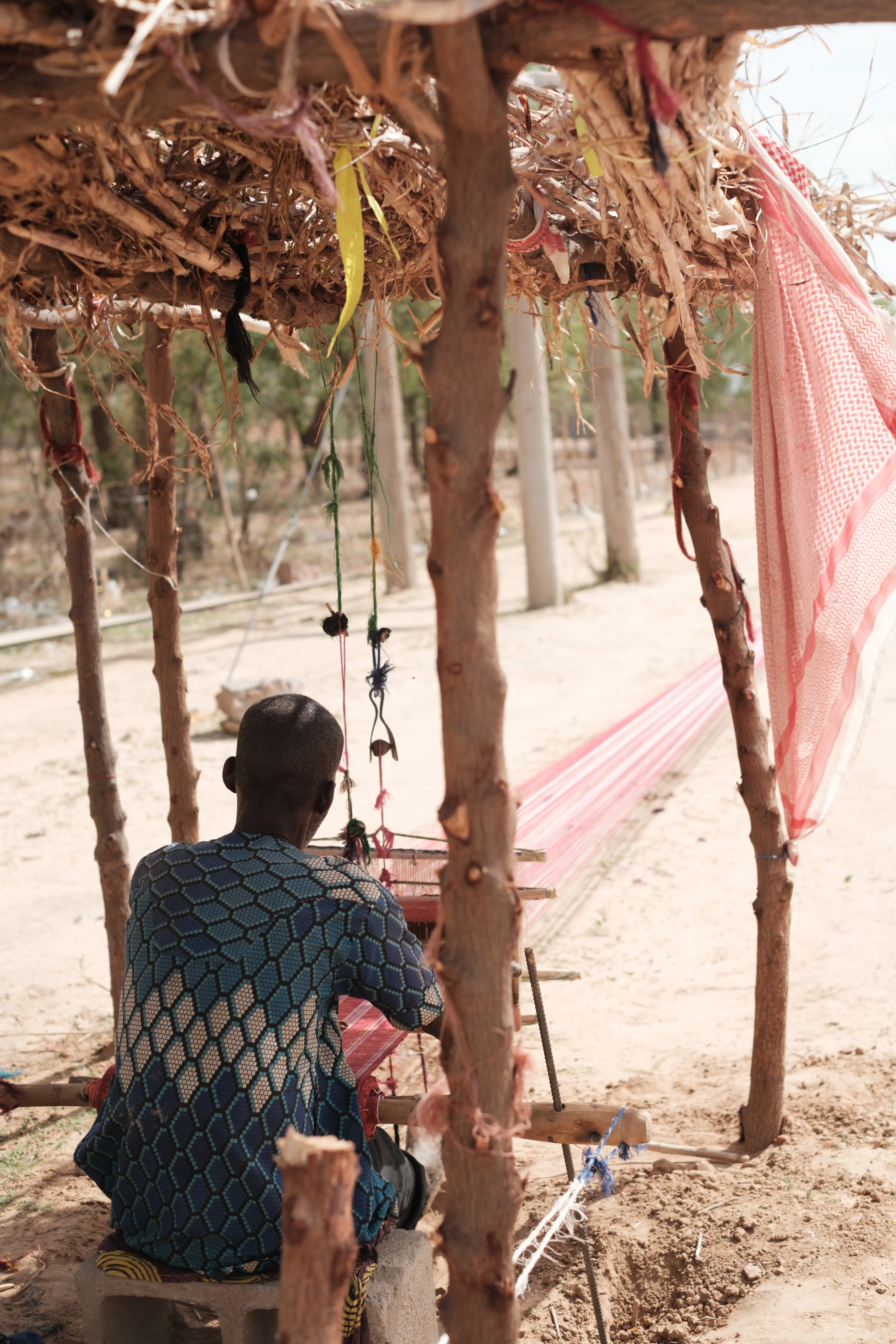 Weaver guiding indigo threads across a loom in Kano